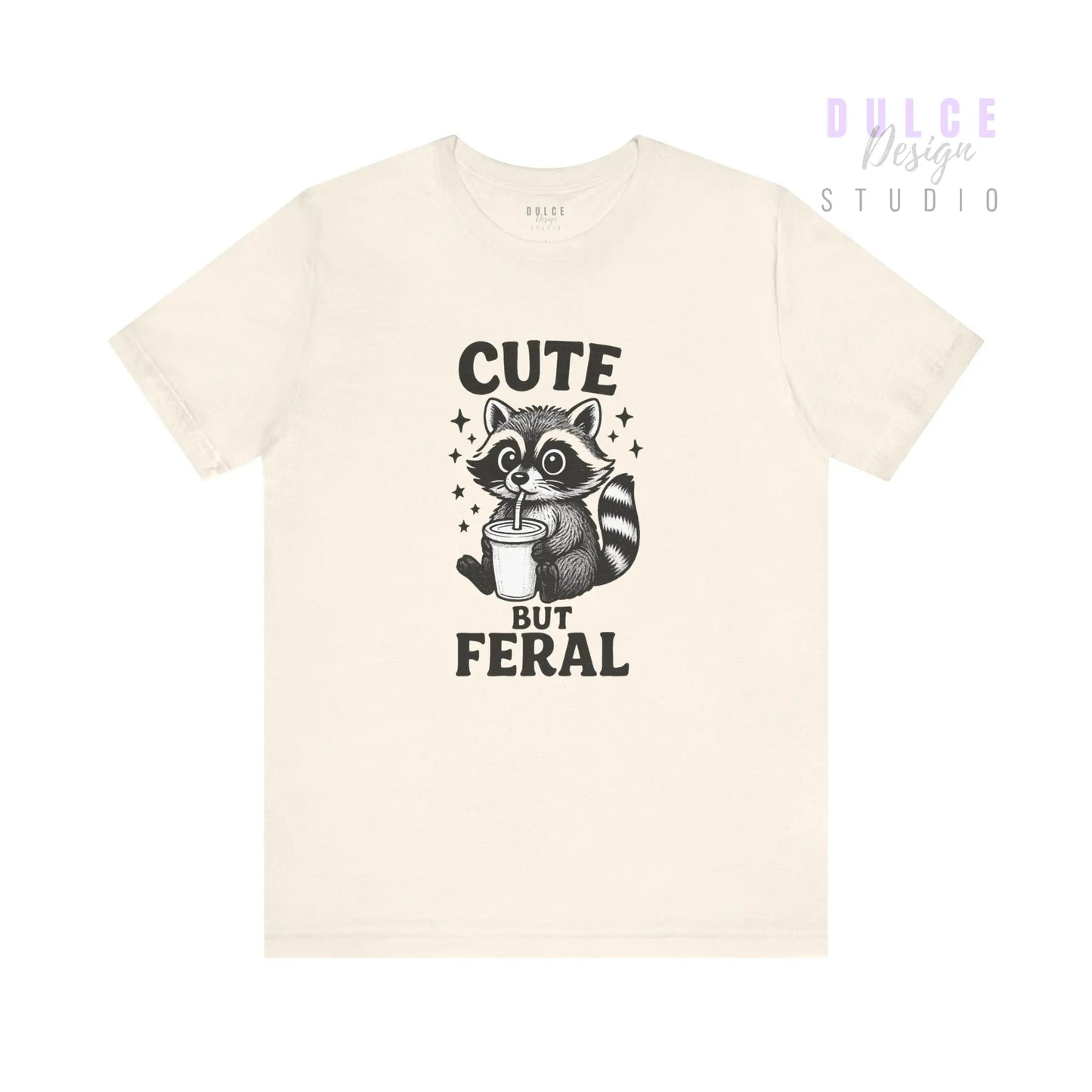 Beige t-shirt with a raccoon graphic and text 'Cute But Feral' on a white background