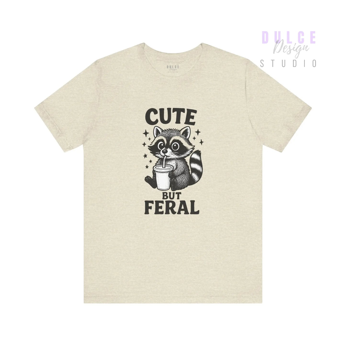 Beige t-shirt with a raccoon graphic and text 'Cute But Feral' on a white background