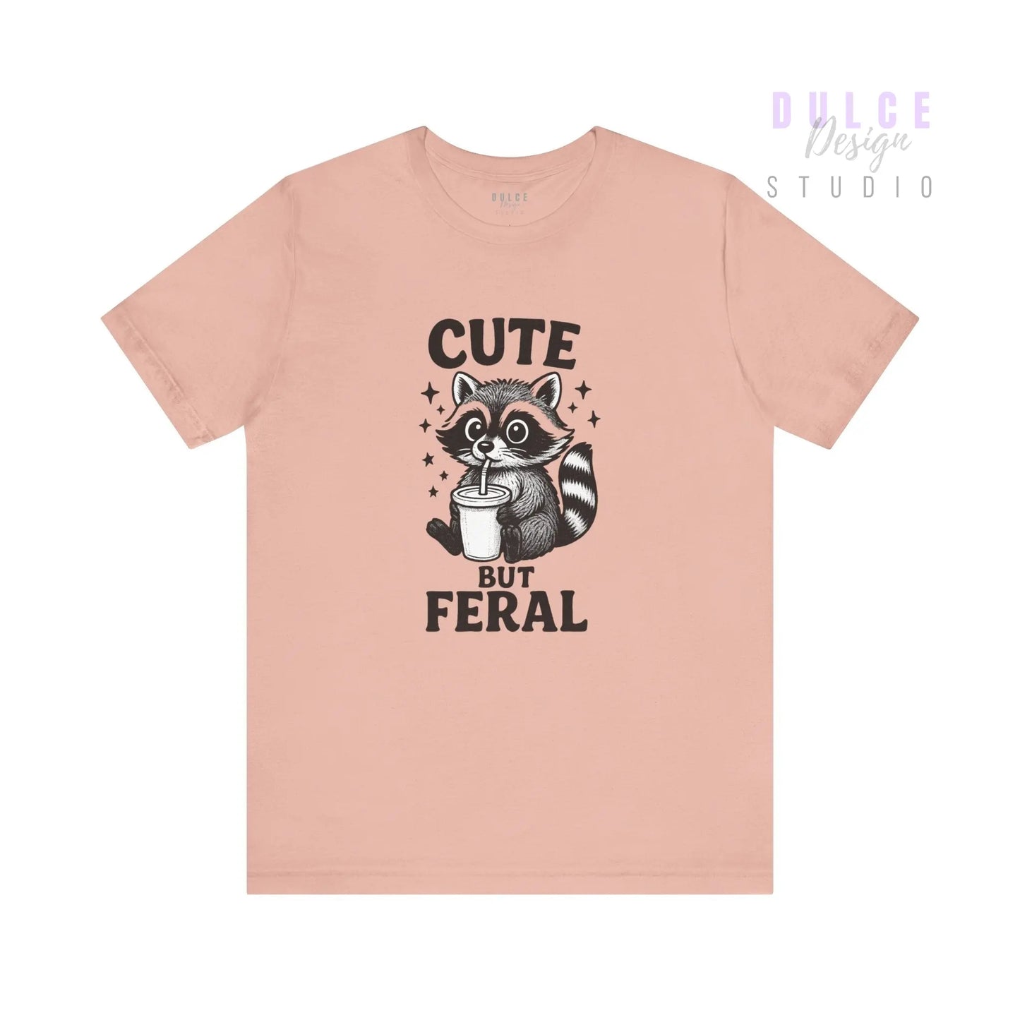 Pink t-shirt with a raccoon graphic and text 'Cute But Feral' on a white background
