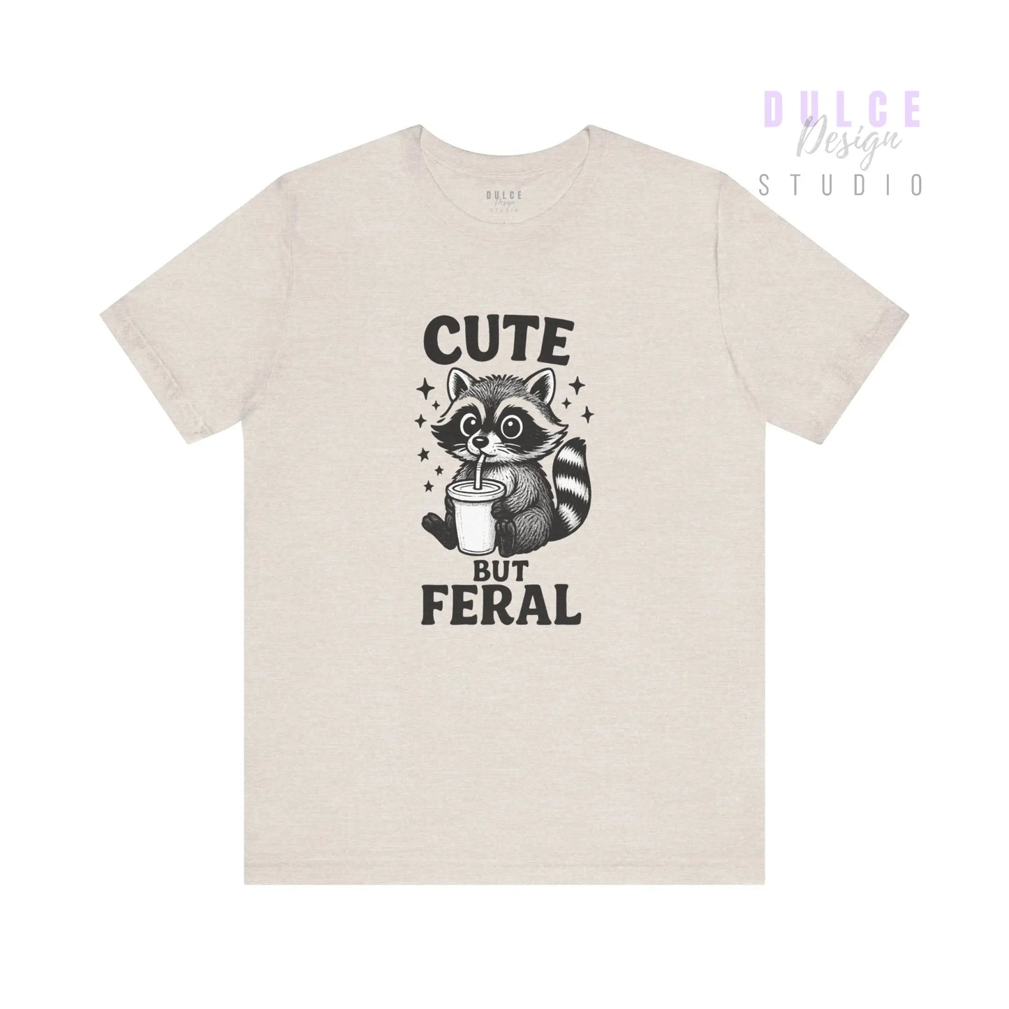 Beige t-shirt with a raccoon graphic and text 'Cute But Feral' on a white background
