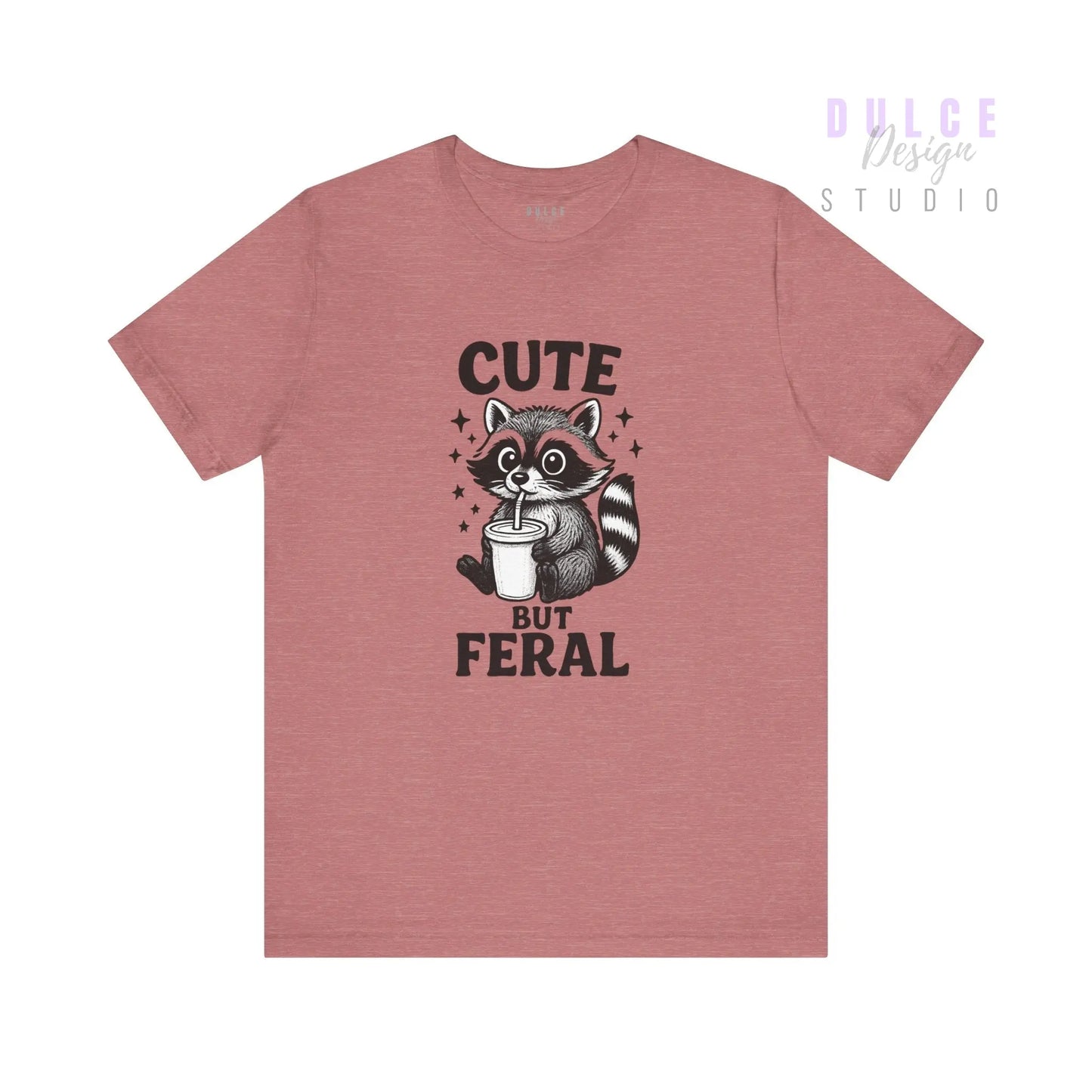 Pink t-shirt with a raccoon graphic and text 'Cute But Feral' on a white background