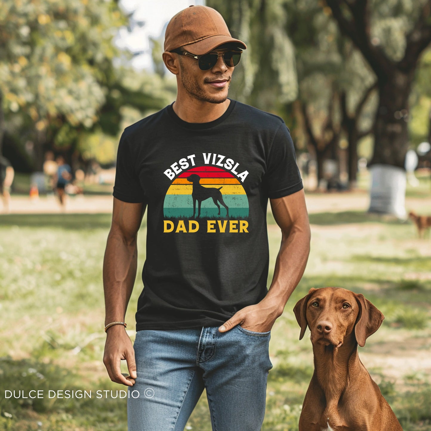 Man wearing "Best Vizsla Dad Ever" retro-style T-shirt with a Vizsla dog by his side in a park setting