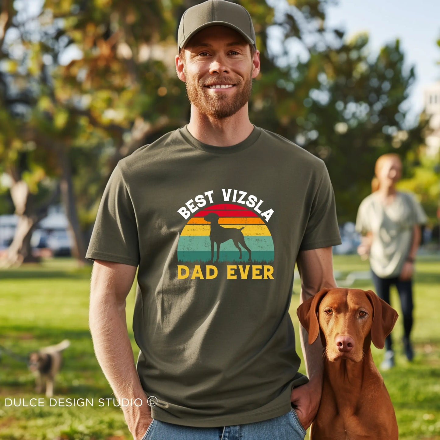 Man wearing "Best Vizsla Dad Ever" retro-style T-shirt with a Vizsla dog by his side in a park setting