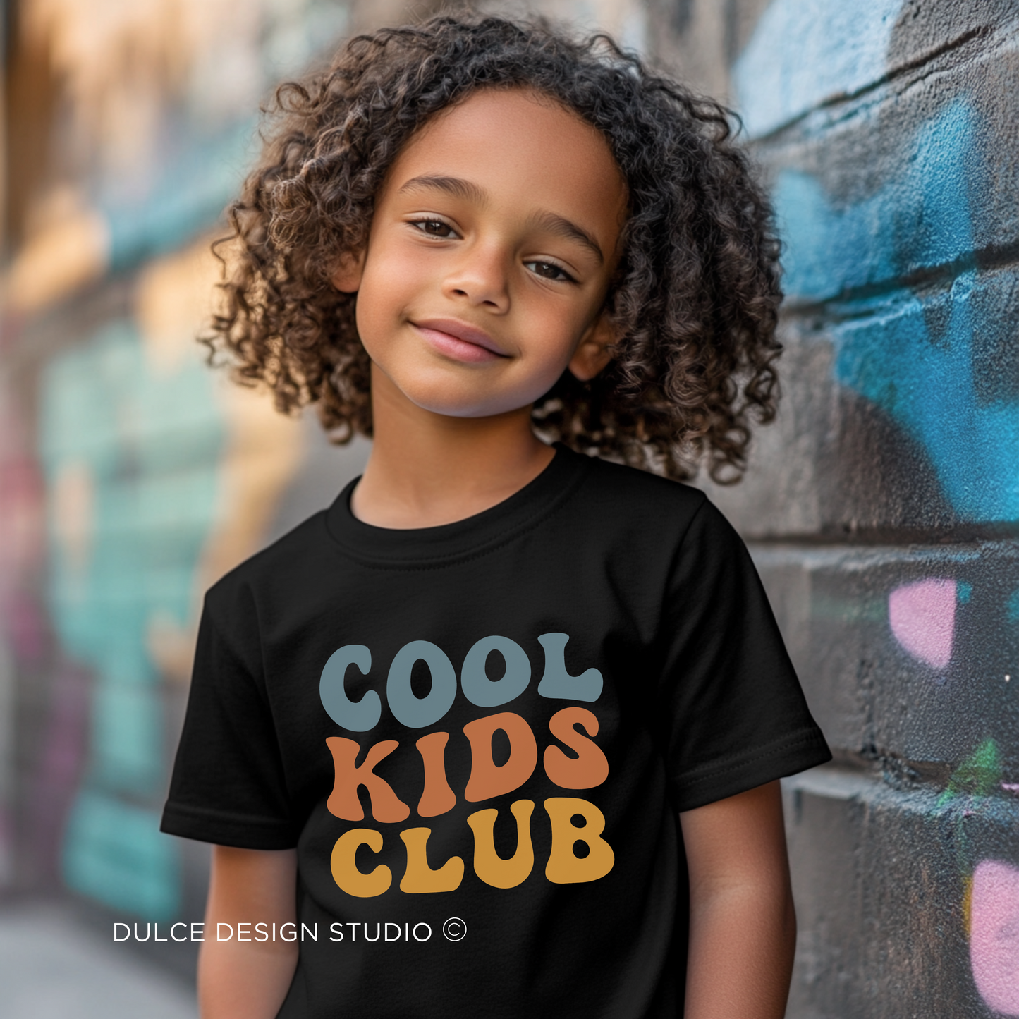 little boy wearing black youth t-shirt with retro rainbow-toned text reading ‘Cool Kids Club’ in large vintage font