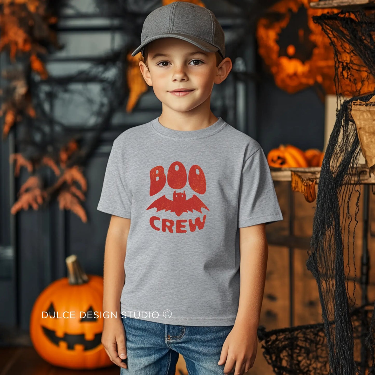 Young boy with gray cap wearing a Boo Crew Unisex Youth Halloween Tee with a playful bat and "Boo Crew" text, ideal for a fun and festive Halloween look.