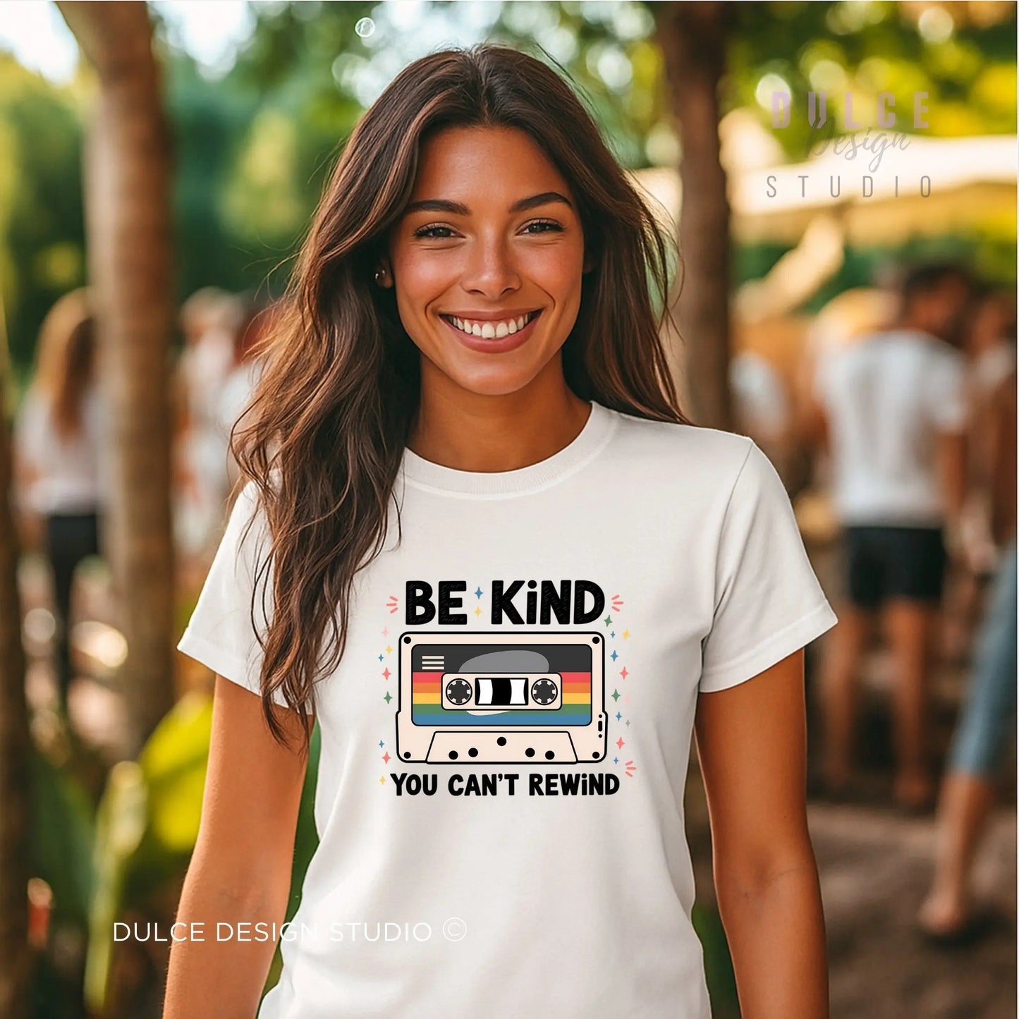 Woman wearing a white t-shirt with 'Be Kind, You Can't Rewind' design outdoors.