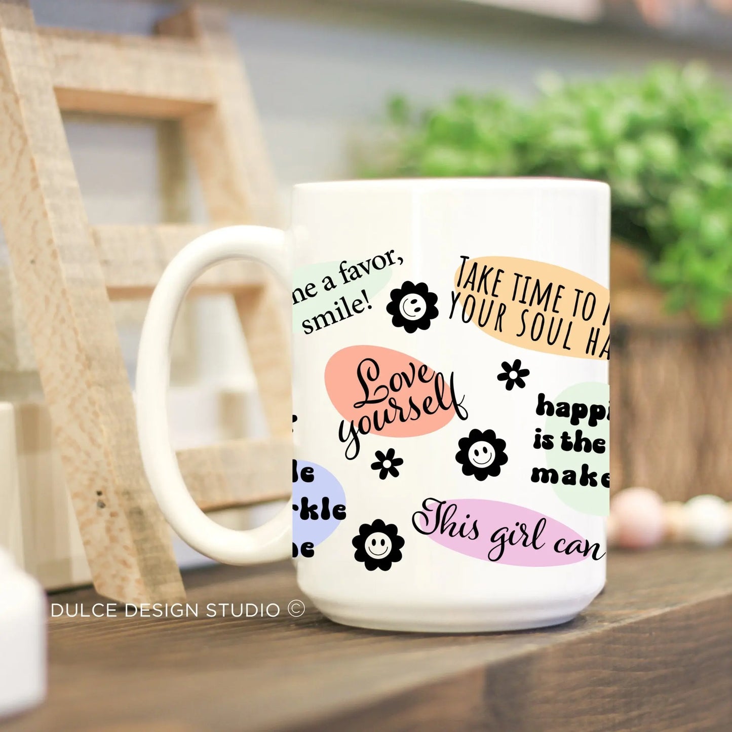 White ceramic mug with pastel-colored retro affirmation phrases and smiley flowers, promoting positivity and self-love