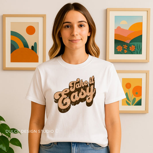 Woman wearing a white t-shirt with 'Take it Easy' text in a casual setting with framed artwork.