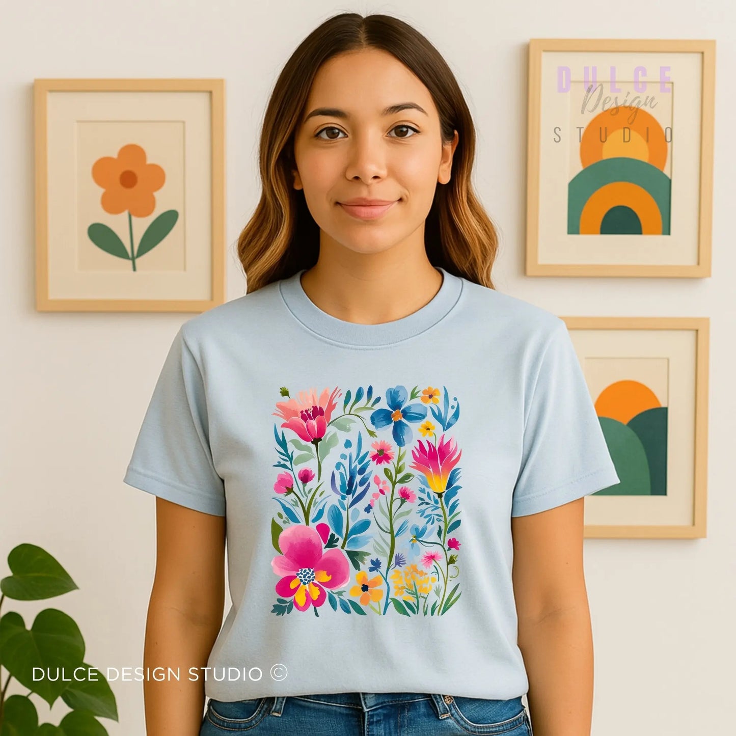 Woman wearing a light blue t-shirt with colorful floral design in front of framed artwork.