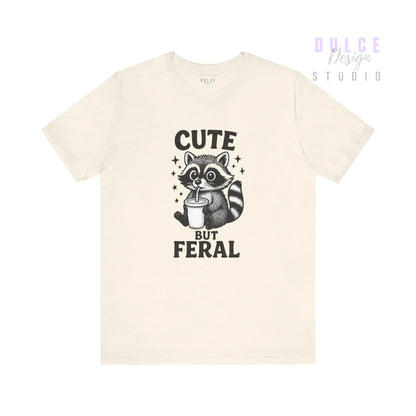 Beige t-shirt with a raccoon graphic and text 'Cute But Feral' on a white background