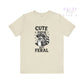 Beige t-shirt with a raccoon graphic and text 'Cute But Feral' on a white background