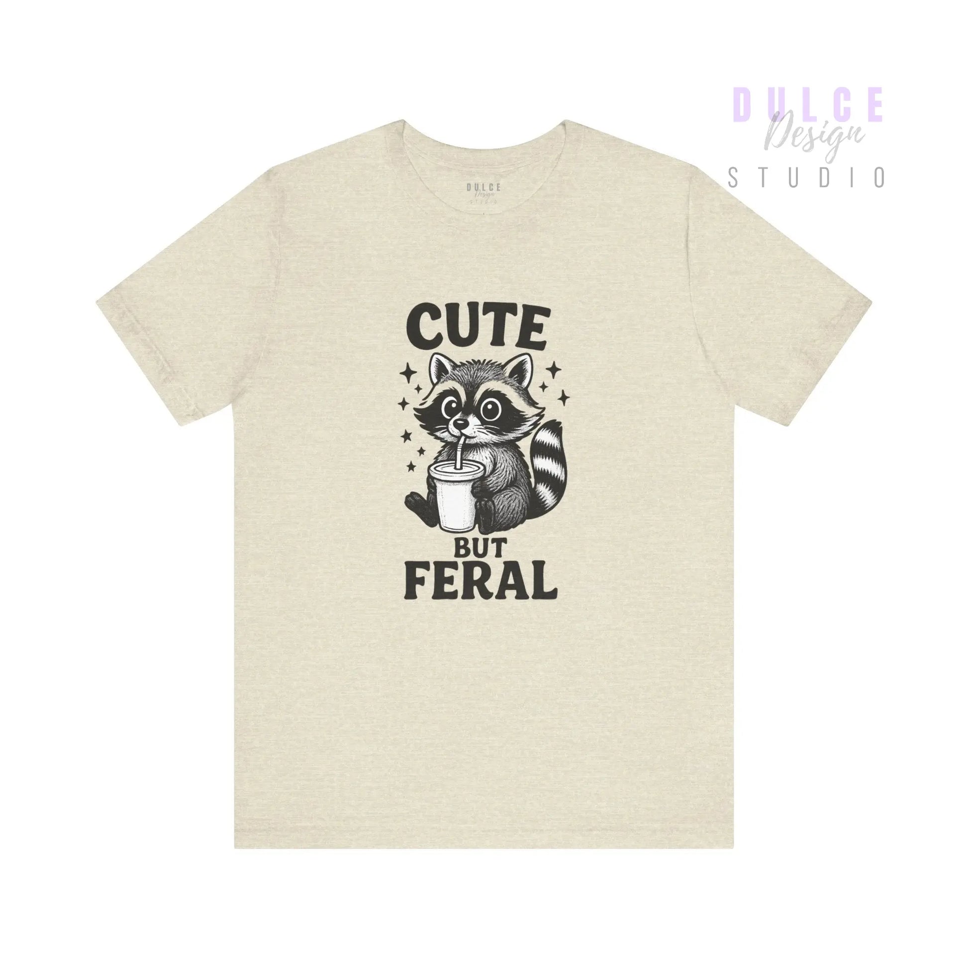 Beige t-shirt with a raccoon graphic and text 'Cute But Feral' on a white background