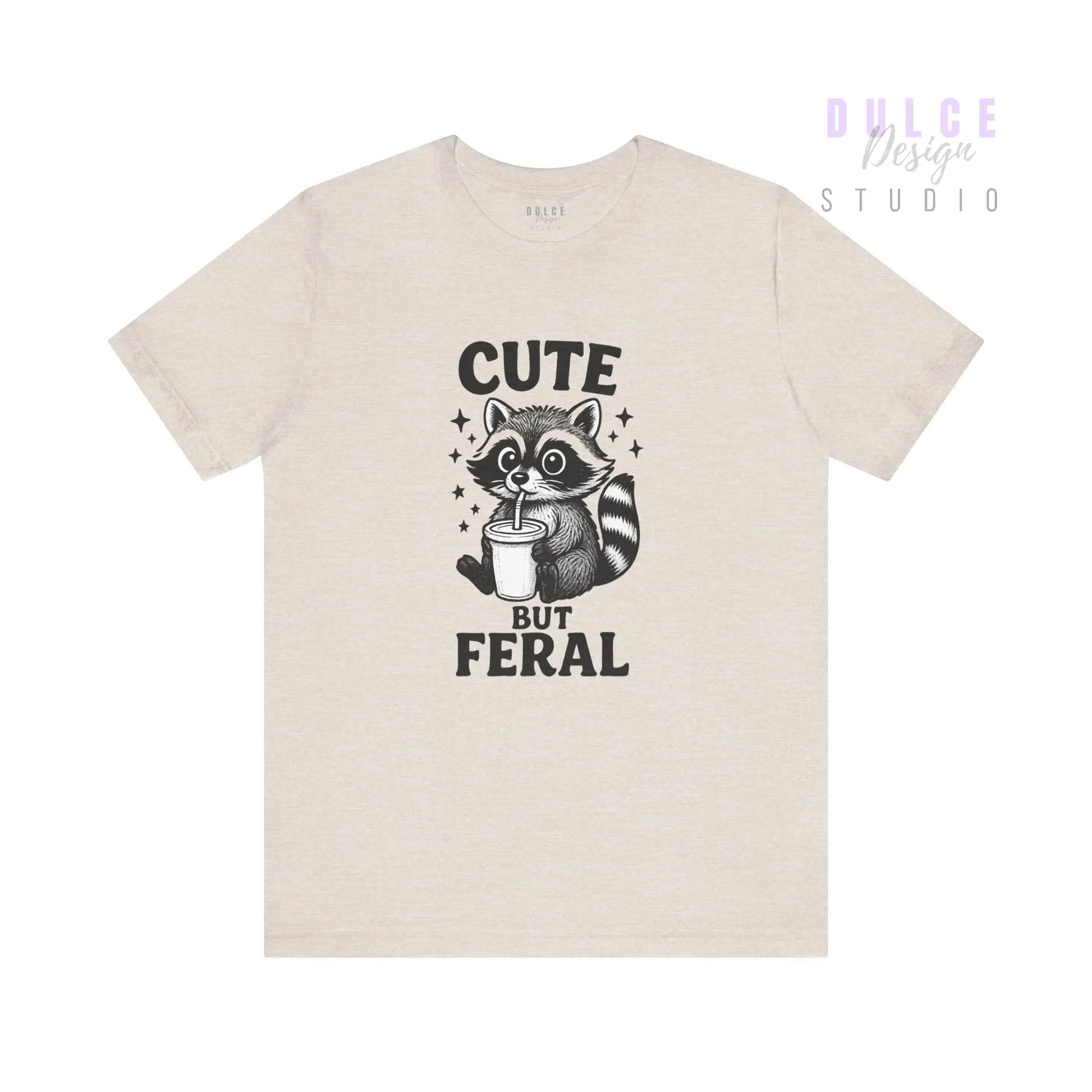 Beige t-shirt with a raccoon graphic and text 'Cute But Feral' on a white background