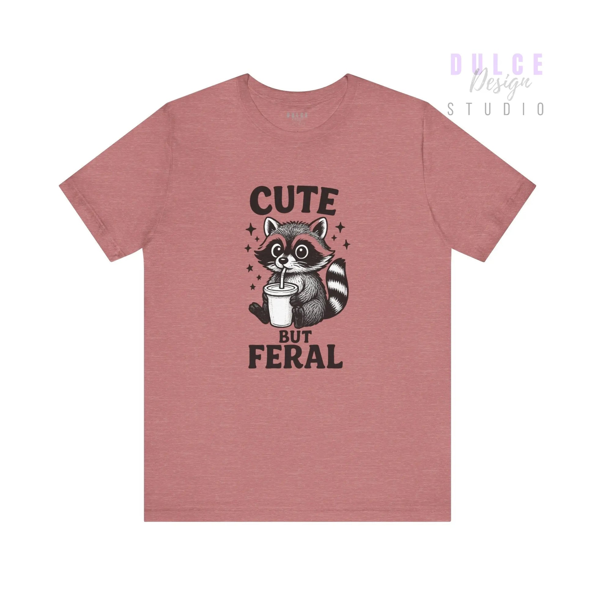 Pink t-shirt with a raccoon graphic and text 'Cute But Feral' on a white background