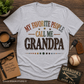 Gray t-shirt with 'My Favorite People Call Me Grandpa' text on a wooden surface with coffee, glasses, and baseball.