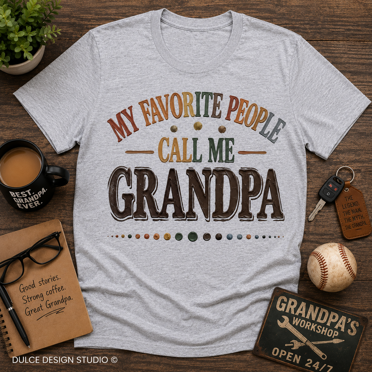 Gray t-shirt with 'My Favorite People Call Me Grandpa' text on a wooden surface with coffee, glasses, and baseball.