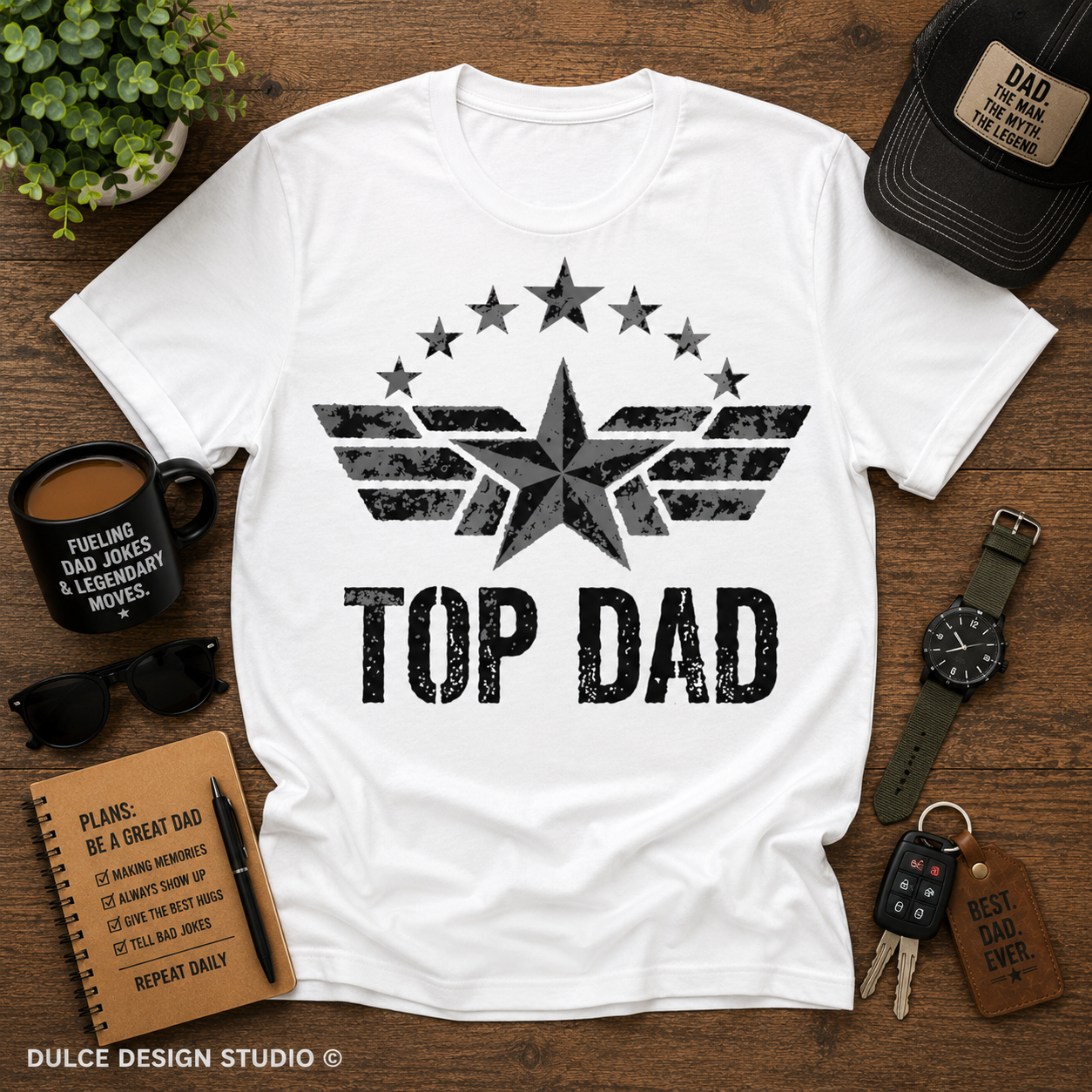 White t-shirt with 'Top Dad' design on a wooden surface with accessories.