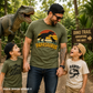 Man and two children in a dinosaur-themed park wearing matching t-shirts with dinosaur graphics.