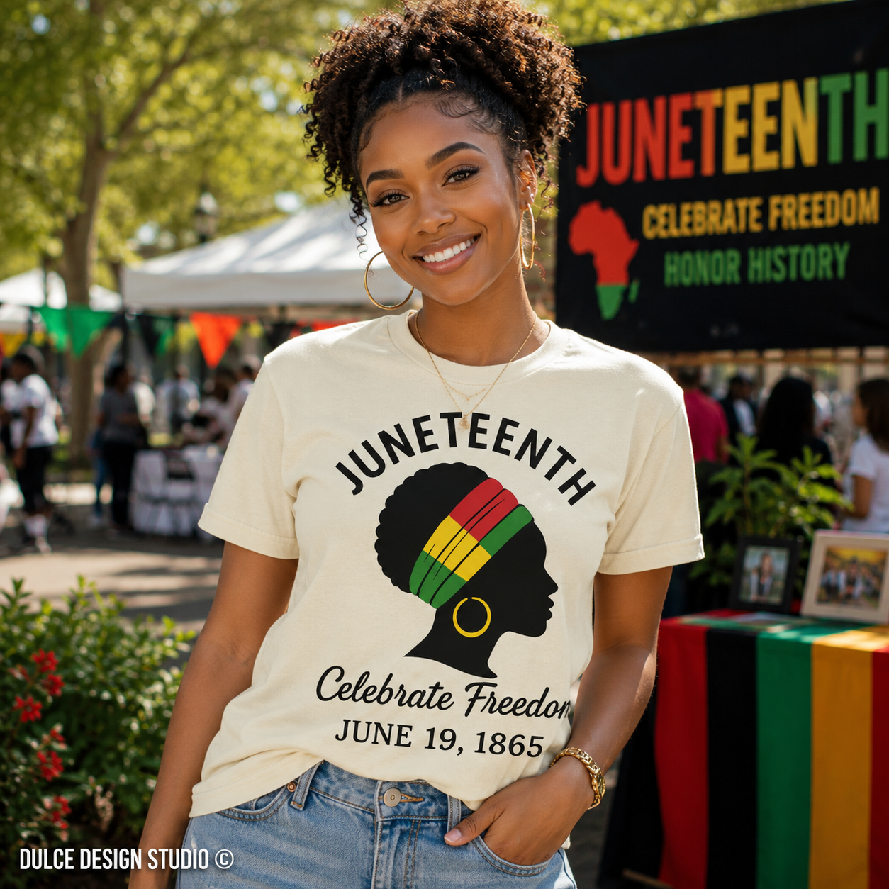 Woman wearing a Juneteenth t-shirt with a colorful design, standing in front of a Juneteenth celebration backdrop.