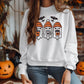 Person wearing a white sweatshirt with a design featuring three ghosts holding coffee cups, wearing orange beanies, and surrounded by bats