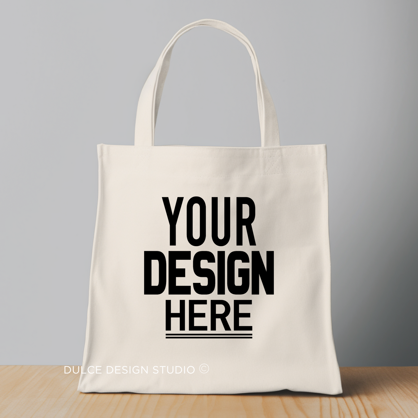 Beige tote bag with "Your Design Here" text in bold black letters
