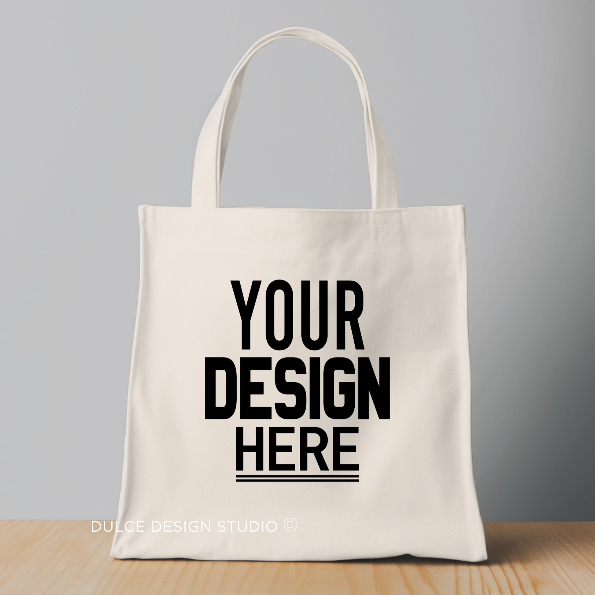 Beige tote bag with "Your Design Here" text in bold black letters