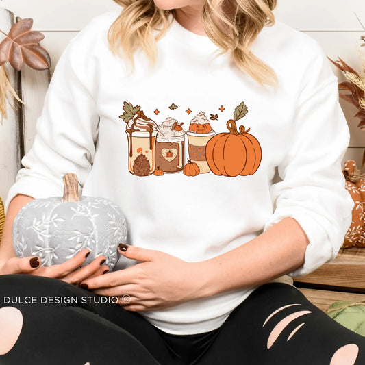 Person wearing a white sweatshirt with a cute design of various fall-themed lattes and pumpkins
