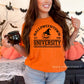 Person wearing an orange t-shirt with a "Halloweentown University" design featuring a jack-o'-lantern and witch hat