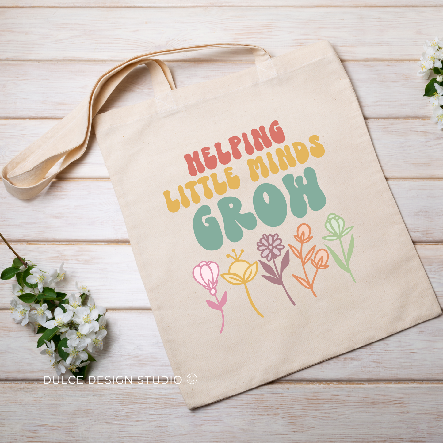 Beige tote bag with the text "Helping Little Minds Grow" in colorful letters and flower illustrations