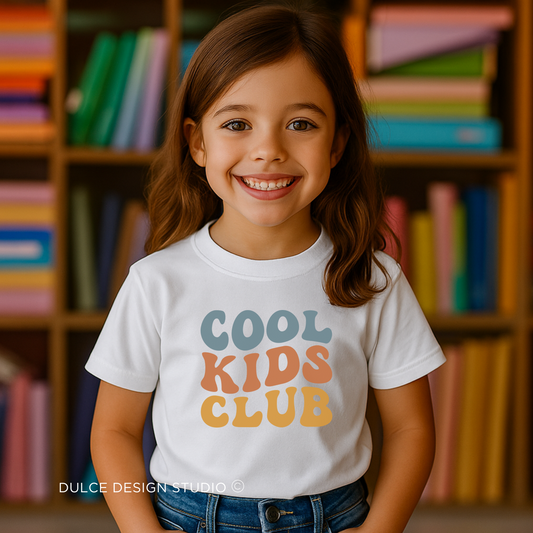 little girl wearing White youth t-shirt with retro rainbow-toned text reading ‘Cool Kids Club’ in large vintage font