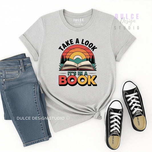 Gray t-shirt with 'Take a Look, It's in a Book' design, paired with jeans and black sneakers on a white background.