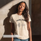 Woman wearing a beige t-shirt with 'Valerie Thomas' design against a textured wall.