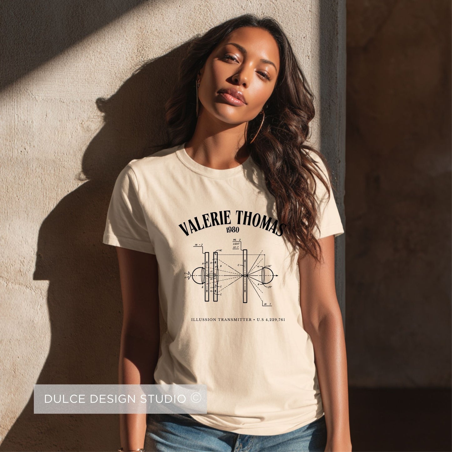 Woman wearing a beige t-shirt with 'Valerie Thomas' design against a textured wall.