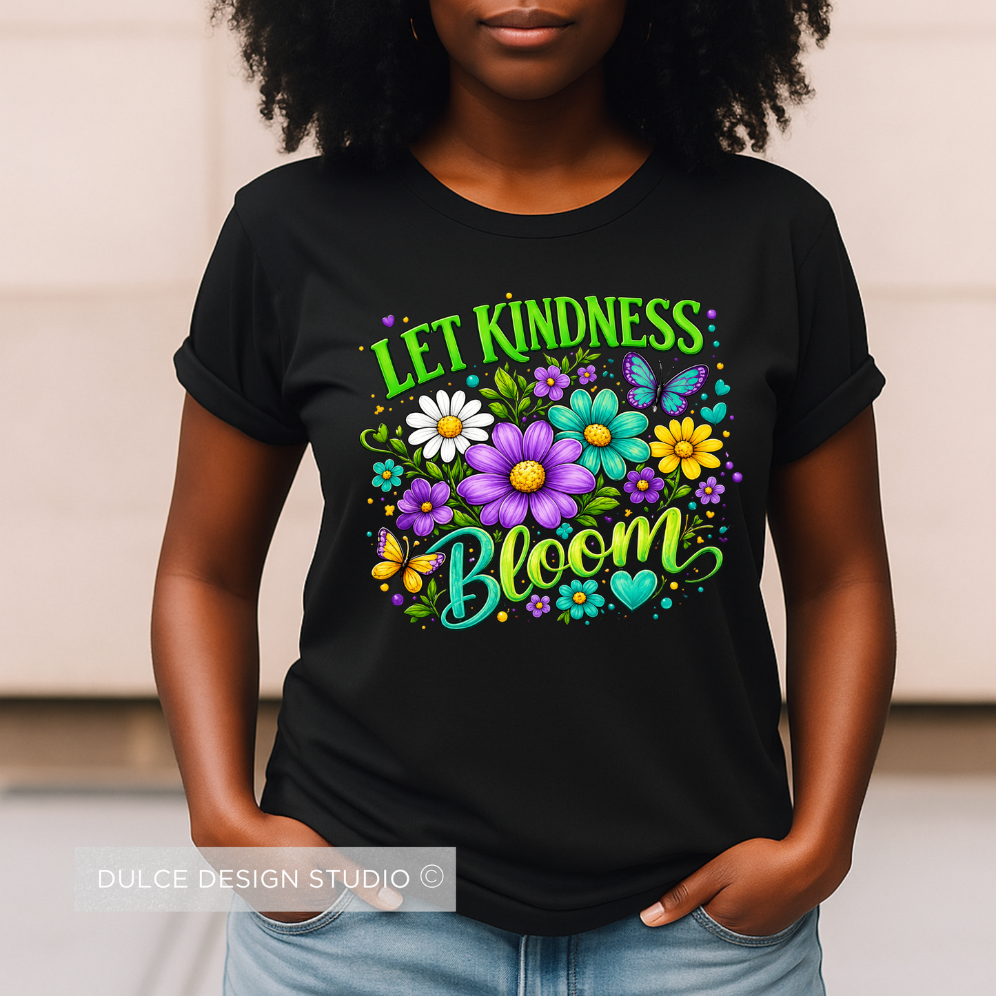 Person wearing a black t-shirt with colorful floral design and 'Let Kindness Bloom' text.
