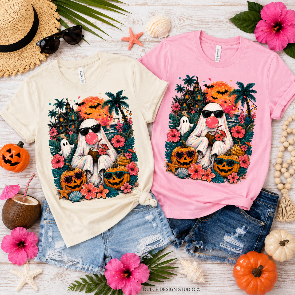Two graphic t-shirts, one cream and one pink, featuring a cartoon ghost with a pink nose in a Halloween tropical setting, styled in a flat lay with denim shorts and autumn props.