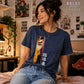 A woman wearing a navy blue graphic t-shirt with a colorful anime-style print of a character and Japanese text, sitting in a cozy, decorated room. The brand logo 'Dulce Design Studio' is visible in the top right and bottom left.