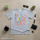 Gray t-shirt with 'Best Dad Ever' text and graphics on a beige surface with accessories.