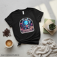 Black t-shirt with a colorful graphic design on a light gray surface with coffee and books.
