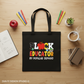 Black tote bag with colorful text on a wooden table with stationery items.