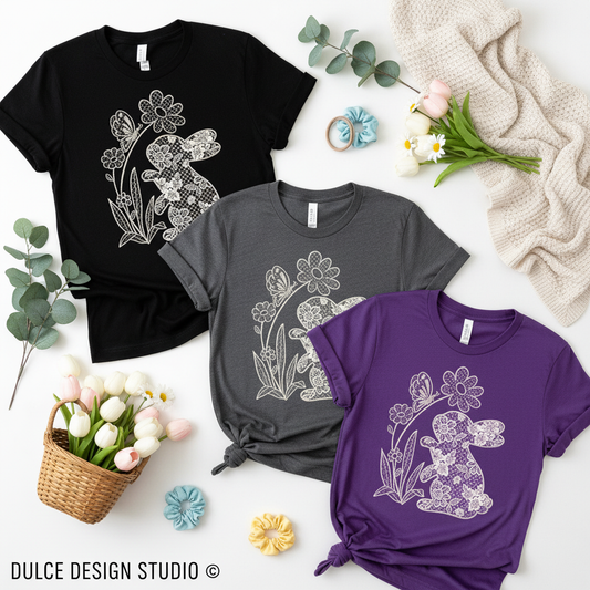 Three t-shirts in black, gray, and purple with floral and bunny designs on a white surface with decorative items.
