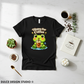 Black t-shirt with a frog holding a coffee cup graphic on a white surface with coffee-related items.