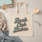 Tote bag with 'Book Club Babes' text on a light surface with glasses and a candle.