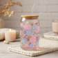 Glass jar with floral design and bamboo lid on a textured surface with candles and books in the background.