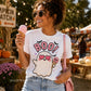 A woman at an outdoor autumn market wearing a white graphic t-shirt with a cute ghost holding a pink ice cream cone and the word 'BOO!' in pink. She is holding a pink ice cream cone and wearing a pink shoulder bag.
