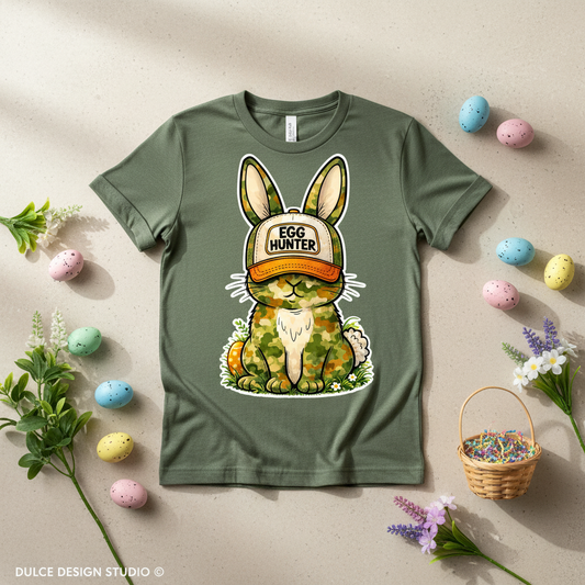 Green t-shirt with a bunny graphic and 'Egg Hunter' cap, surrounded by Easter decorations on a beige background.