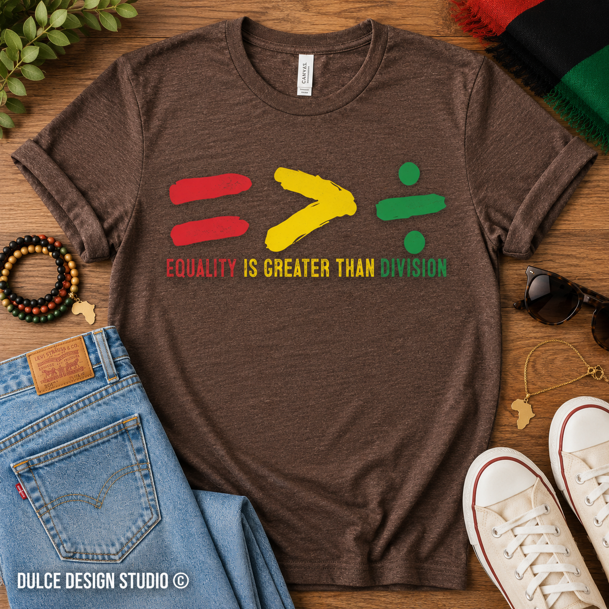 Brown t-shirt with colorful equality symbol design on a wooden surface with jeans and sneakers.