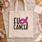 A beige canvas tote bag laid flat on a linen cloth over a wooden surface, printed with the words 'FU CANCER' in black and a bright pink ribbon graphic. Pink flowers, a small card, and a pink ribbon are arranged around it.