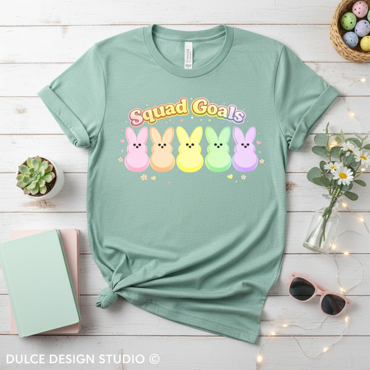 Mint green t-shirt with Peeps characters and 'Squad Goals' text on a wooden surface with decorative items.