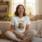 Woman sitting on a couch holding a mug, wearing a t-shirt with a graphic and text.