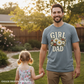 Man wearing a 'Girl Dad' t-shirt holding hands with a young girl in a garden.